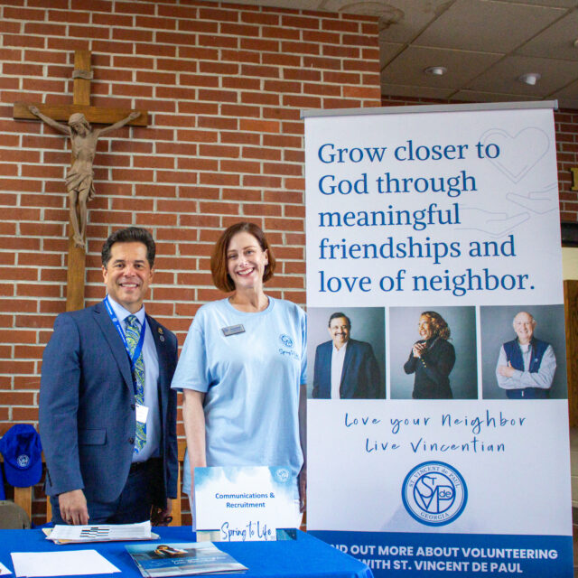 Man and woman standing beside St. Vincent de Paul Georgia banner with large crucifix on wall behind them